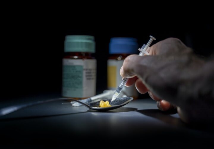 A hand reach for a syringe with medication bottles in the background