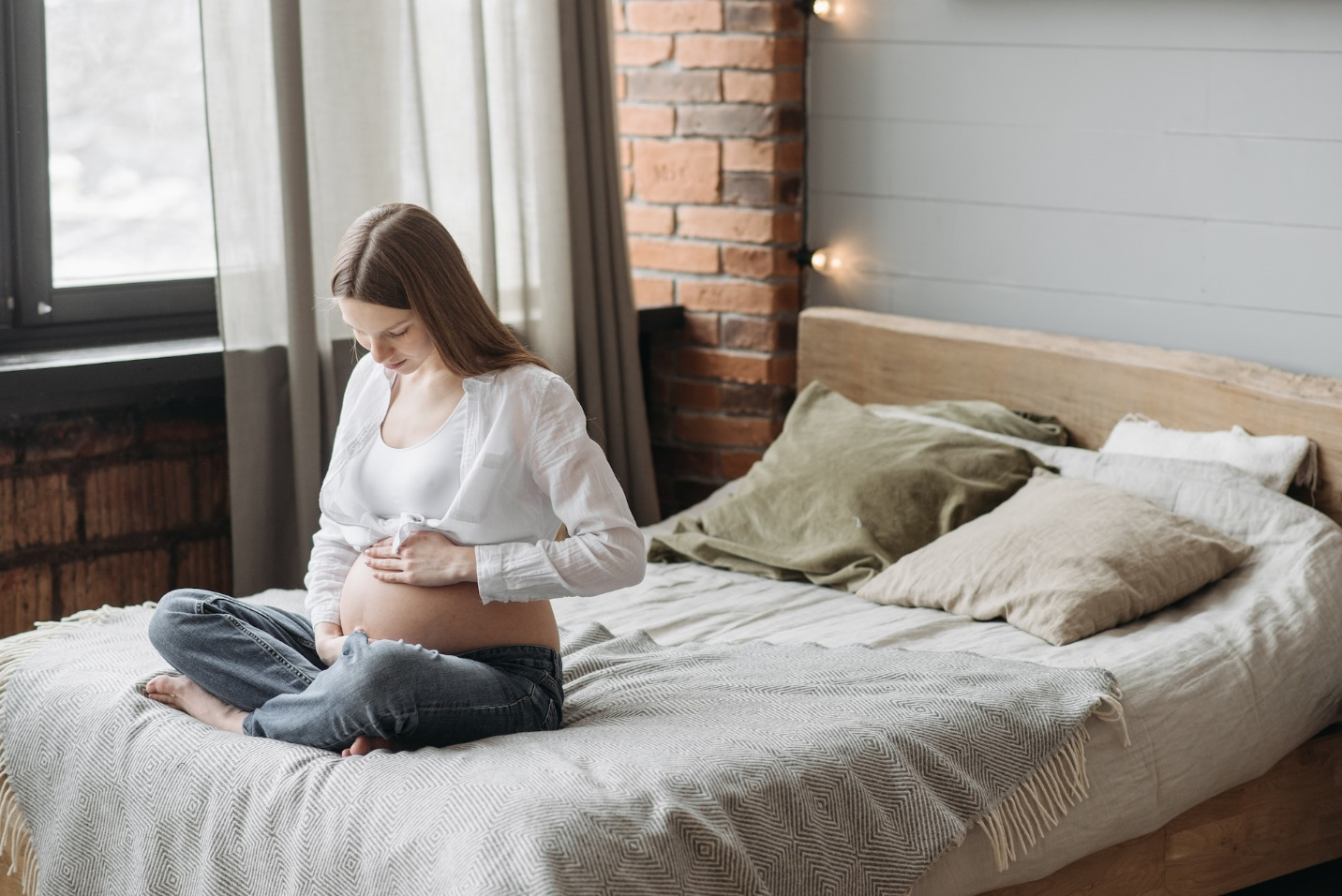 Pregnant Woman Holding Her Belly Sitting On a Bed