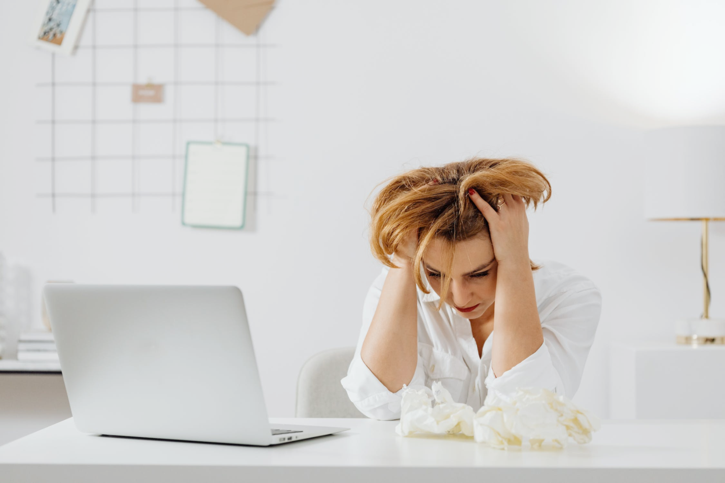 An image of a woman sitting in front of a laptop holding her head